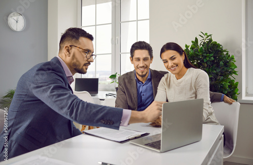 Real estate agent consulting family couple about mortgage or rent. Insurance broker or salesman making offer to young couple using laptop. Smiling husband and wife looking at laptop screen
