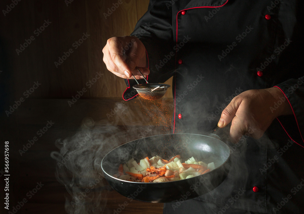 The chef adds paprika to fried carrots and onions in a frying pan. Cooking vegetables for lunch. Restaurant or hotel menu on a dark background The chef adds paprika to fried carrots and onions in a frying pan. Cooking vegetables for lunch. Restaurant or hotel menu on a dark background