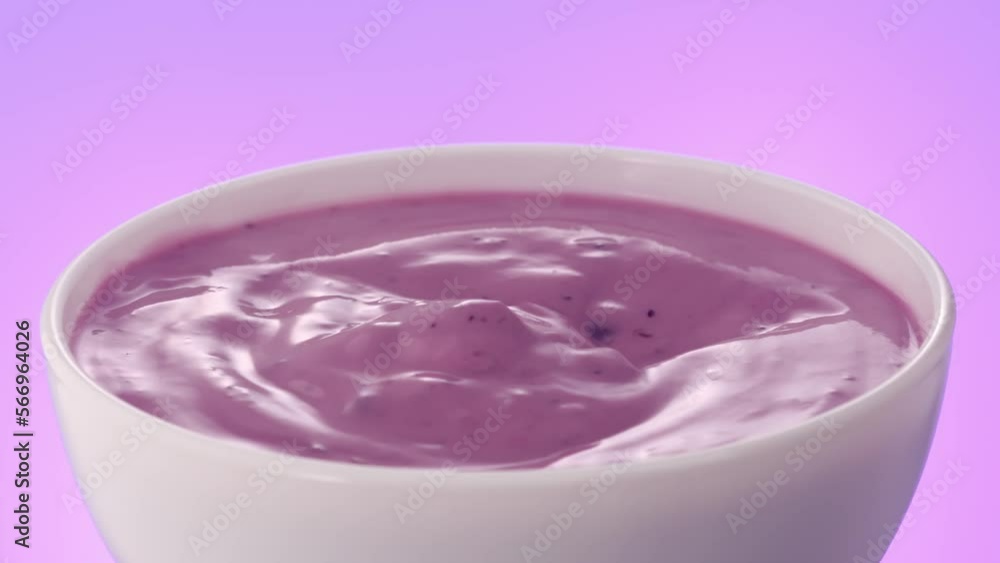 Spoon takes berry yogurt from a white bowl rotates on a colored background. blueberry cream closeup. High quality 4k footage Spoon takes berry yogurt from a white bowl rotates on a colored background. blueberry cream closeup. High quality 4k footage