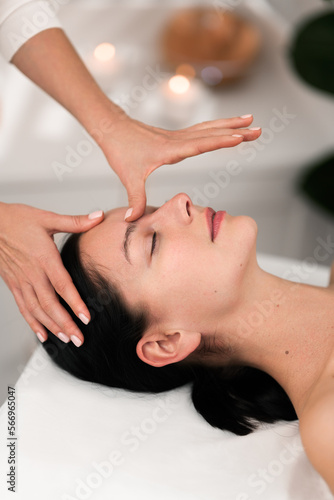 Crop masseuse doing acupressure facial massage to female client