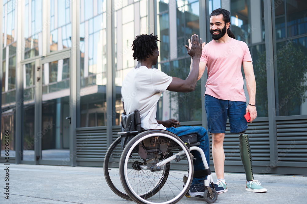 A pair of disabled friends on vacation having fun and breaking down barriers. They share a moment of joy high-fiving each other in celebration of their friendship. A pair of disabled friends on vacation having fun and breaking down barriers. They share a moment of joy high-fiving each other in celebration of their friendship.
