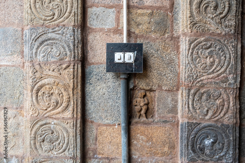 An electric switch board between carved columns on the stone wall of an ancient Hindu temple.