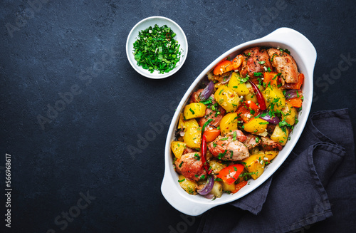 Baked turkey drumsticks fillet with potatoes, paprika, onions, herbs and spices in baking dish, black table background, top view