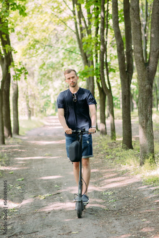 Fototapeta premium Young man rides on electric scooter in park.