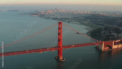 Wide circling aerial shot of the golden gate bridge at sunset with San Francisco skyline in the background