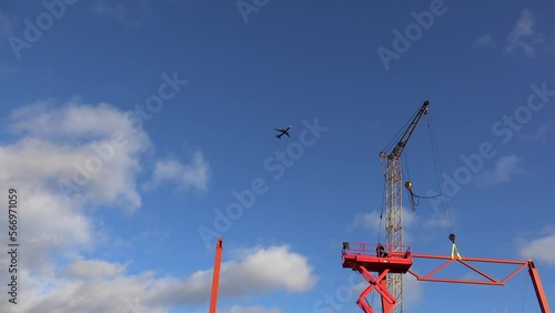 Plane flies over the construction site with a crane, metal structures, workers on a scissor lift.