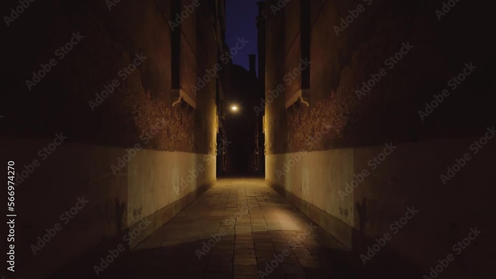 Dark street between old buildings in Venice at night with an illuminated lighthouse Dark street between old buildings in Venice at night with an illuminated lighthouse