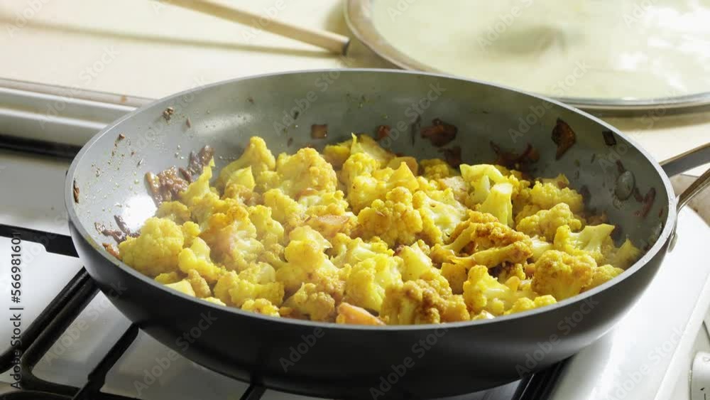 The camera zooms slowly on curried cauliflower florets steaming in a non-stick frying pan on the gas. The camera zooms slowly on curried cauliflower florets steaming in a non-stick frying pan on the gas.