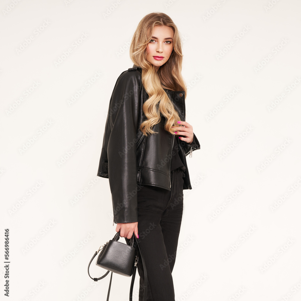 Fototapeta premium Young blonde woman in black leather jacket and black jeans. Girl posing on a white background. Jewelry and hairstyle. Fashion photo
