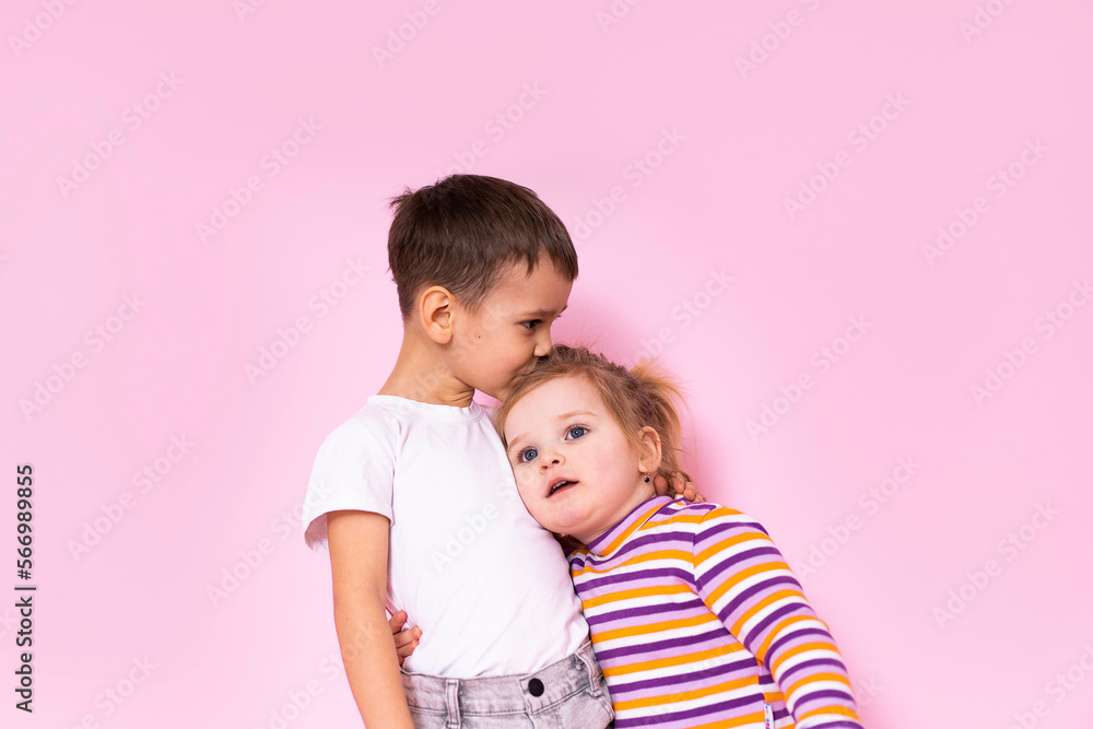 cute kids hugging on a pink background. The brother kisses his younger sister on the head. cute kids hugging on a pink background. The brother kisses his younger sister on the head.
