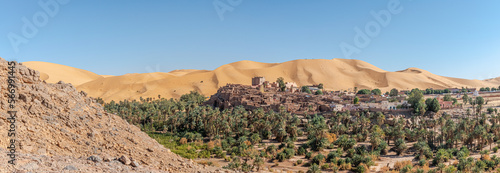 Panoramic view of Taghit in Bechar. Algerian Sahara desert oasis palm trees, trees, sand dunes and ksar old dry stone buildings. Aerial view from rocky mountain Djebel Baroun in foreground.  photo