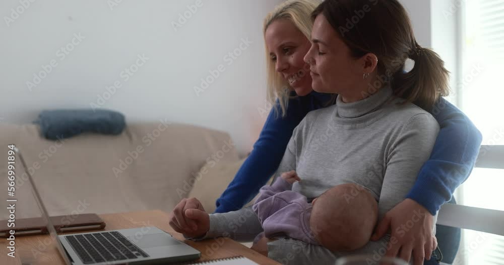Young mothers using laptop at home while feeding her infant son - Smart working and family concept Young mothers using laptop at home while feeding her infant son - Smart working and family concept
