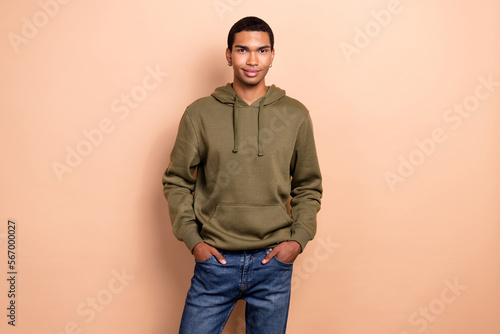 Photo of young hipster positive guy wear piercing stylish outfit khaki hoodie with jeans posing model satisfied isolated on beige color background