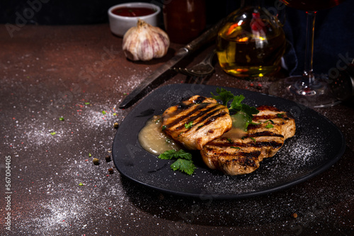 American bbq food concept. Grilled barbeque pork meat steaks with traditional gravy sauce, spices and greens, on plate board, dark background top view copy space 