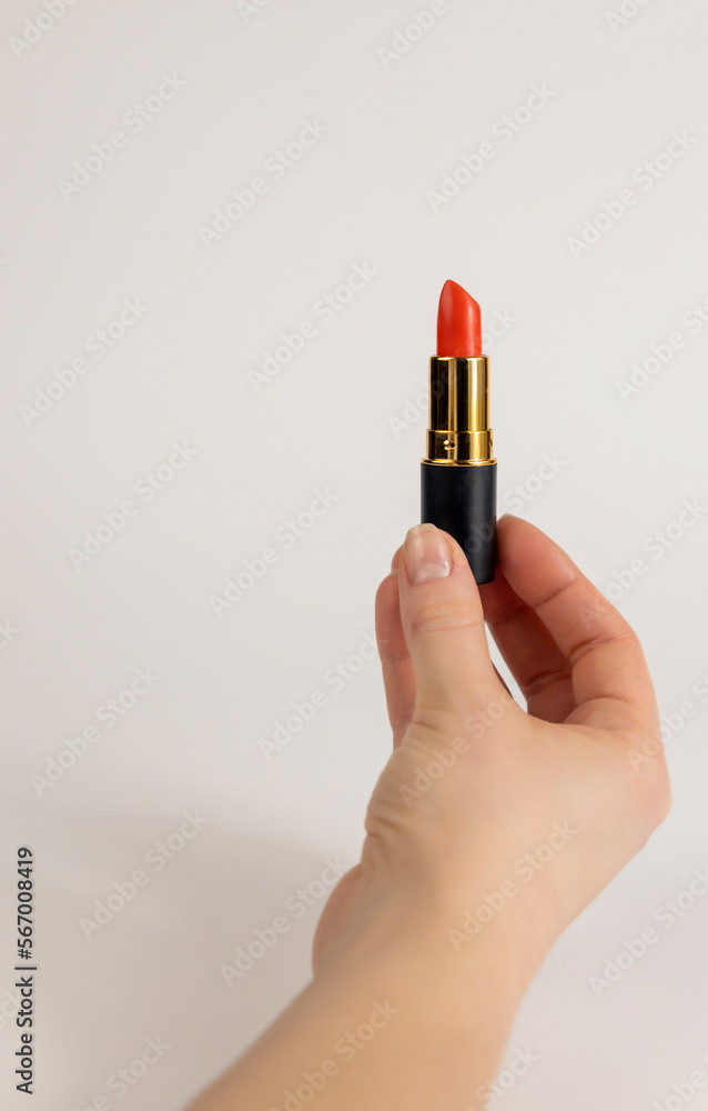 A woman's hand holds red lipstick. Close up on a white background.