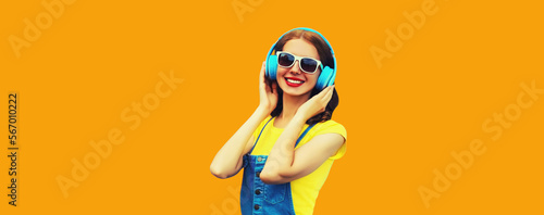 Portrait of happy smiling young woman with headphones listening to music on yellow background © rohappy