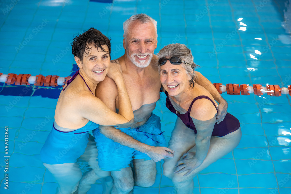 Senior man and two women standing in the water at the swimming pool