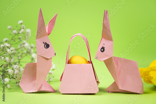 Easter origami - two paper bunnies and an egg, green background. Crafts for the holiday, do it yourself