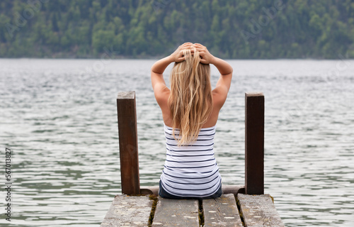 teenage girl sits thouhtfully on the jetty by the water in the summer time, 