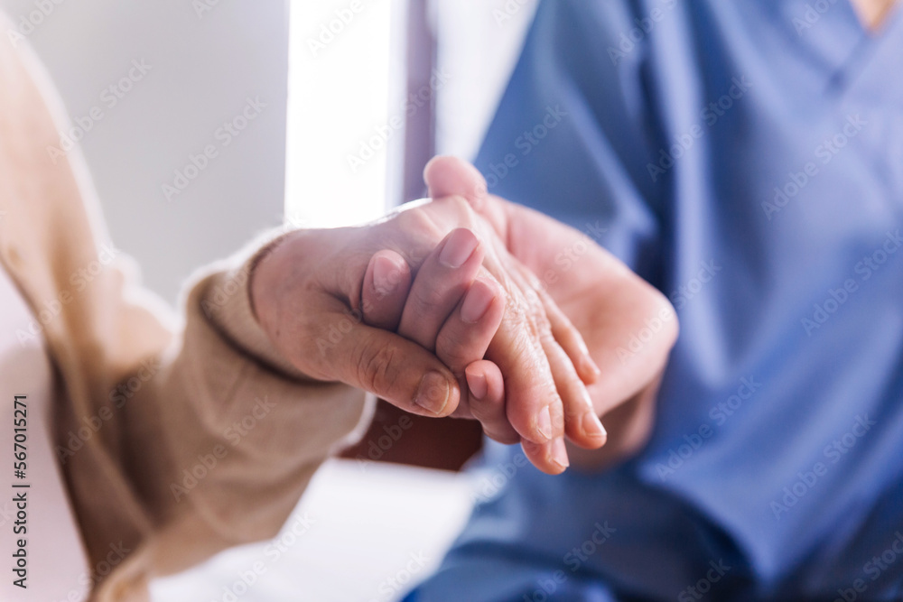 Close-up senior Asian woman hand with her caregiver helping hands holding together, Caregiver visit at home. Home health care and nursing home concept. Close-up senior Asian woman hand with her caregiver helping hands holding together, Caregiver visit at home. Home health care and nursing home concept.