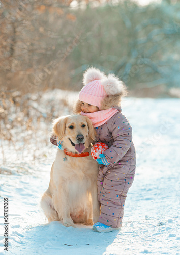 Young girl portrait in pink hat playing active game with her dog golden retriever in winter season