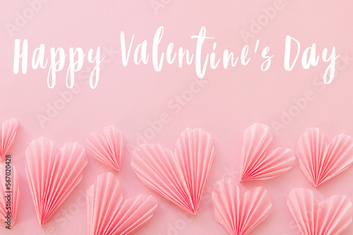 Happy valentines day text on cute pink hearts flat lay on pink paper background. Modern Valentines day greeting card. Handwritten sign. Heart border