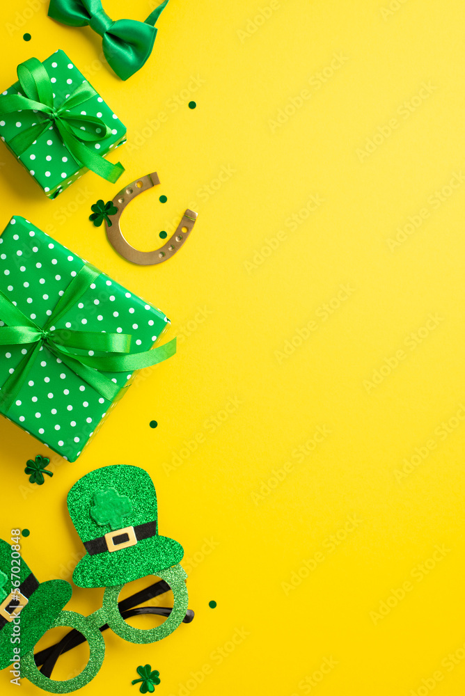 Saint Patrick's Day concept. Top view vertical photo of green gift boxes horseshoe hat shaped party glasses bow-tie and clover shaped confetti on isolated yellow background with empty space