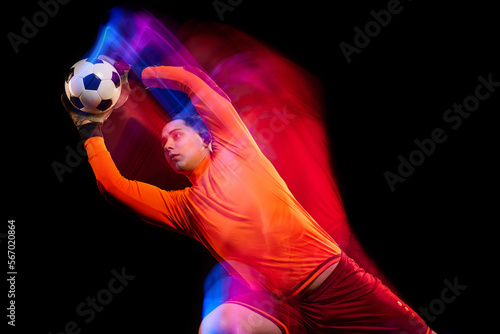Sportive energetic man, soccer football goalkeeper in action, motion over dark background with mixed neon light. Concept of sport, achievement, competition, goals.