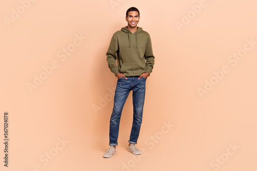 Full length photo of good looking nice man glad man wear khaki trendy outfit stands hands hold pockets isolated on beige color background