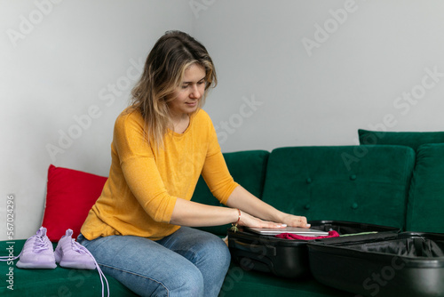 Calm, serious, concentrated blond woman packing clothes in big suitcase on green sofa. Prepare for travelling, ejectment photo