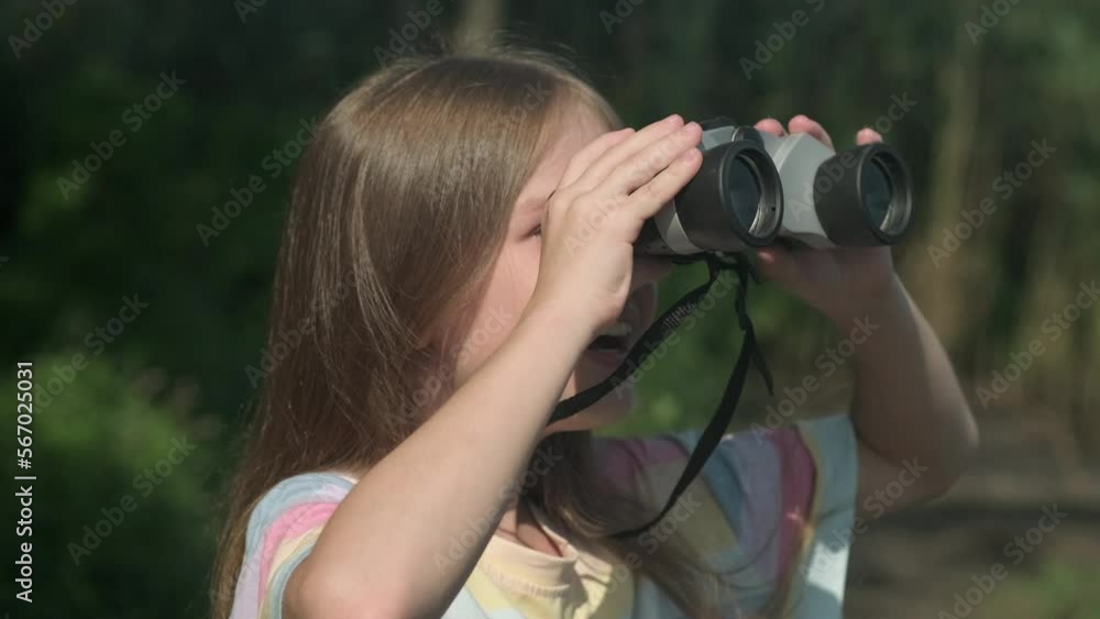 Little girl tourist in the forest looking through binoculars with a surprised face close up. Happy child scout outdoors. Concept of summer camp, adventure, scouting and hiking tourism for kids Little girl tourist in the forest looking through binoculars with a surprised face close up. Happy child scout outdoors. Concept of summer camp, adventure, scouting and hiking tourism for kids