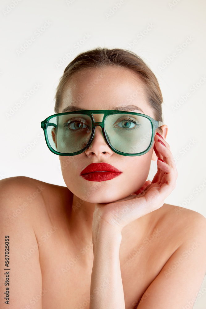 Femininity and sensuality. Young beautiful girl with red lips posing in green sunglases over grey studio background. Concept of natural beauty, skin care, cosmetology, cosmetics, health, fashion