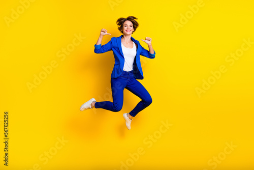Full length photo of cool confident woman wear blue jumping high pointing thumbs herself isolated yellow color background © deagreez