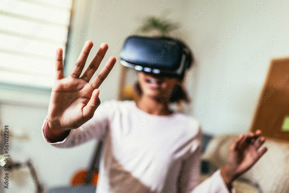 African American girl using virtual reality glasses in her room. Black girl enjoys VR technology to watch 3D movies or immerse herself in metaverse