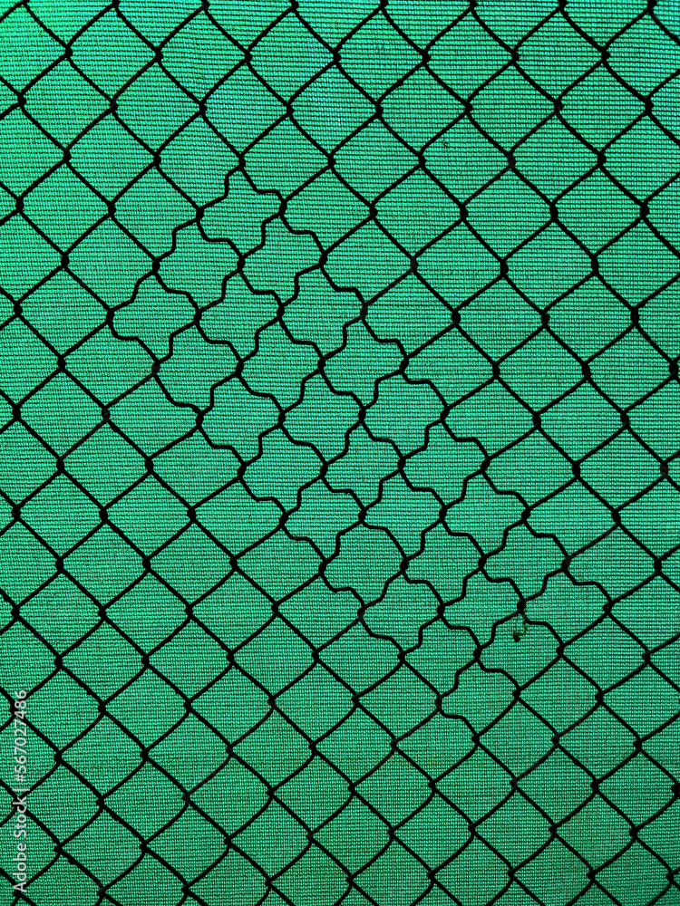 Fototapeta premium Chain-link fencing with the diamond pattern and green fiber screening as background