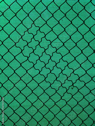 Chain-link fencing with the diamond pattern and green fiber screening as background photo