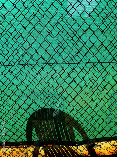 Shadow of a plastic chair on green screening of chain-link fence photo