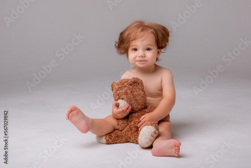 a baby girl in a diaper sits and plays hugs with a teddy bear on a white background