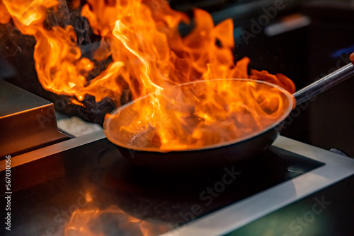 Chef hand in restaurant kitchen with pan, cooking flambe on food