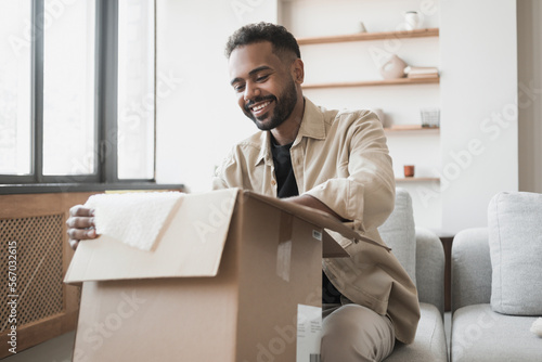 Happy young man opening parcel at home, handsome guy open package indoor, delivery, shipment, satisfied customers concept