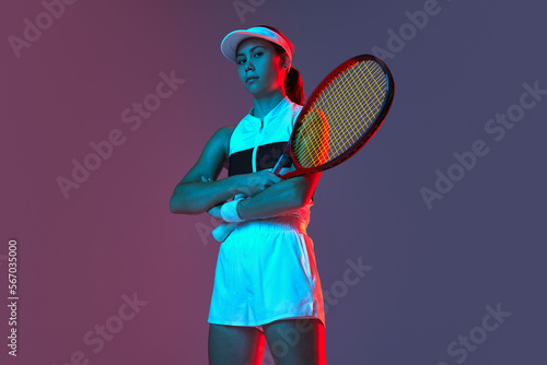 Young sportive girl professional tennis player posing with tennis racket gradient pink-purple background in neon. Concept of sport, strength, professional skills, active lifestyle. © Lustre
