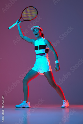 Portrait of young professional female tennis player in sports uniform in motion, action over gradient pink-purple background in neon light. Sport, fashion, energy, motivation concept © Lustre