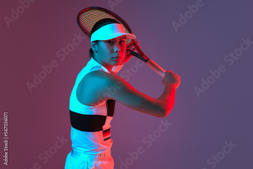 Young sportive girl professional tennis player posing with tennis racket gradient pink-purple background in neon. Concept of sport, strength, professional skills, active lifestyle.