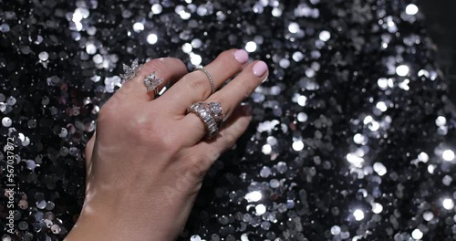 Video of close up elegant hand move fingers with sparkling gems and jewelry rings on black sparkling textile background photo