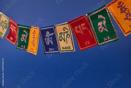 Tibetan Buddhist flags against blue background. Text on flags Om mani padme hum meaning The jewel is in the lotus.
