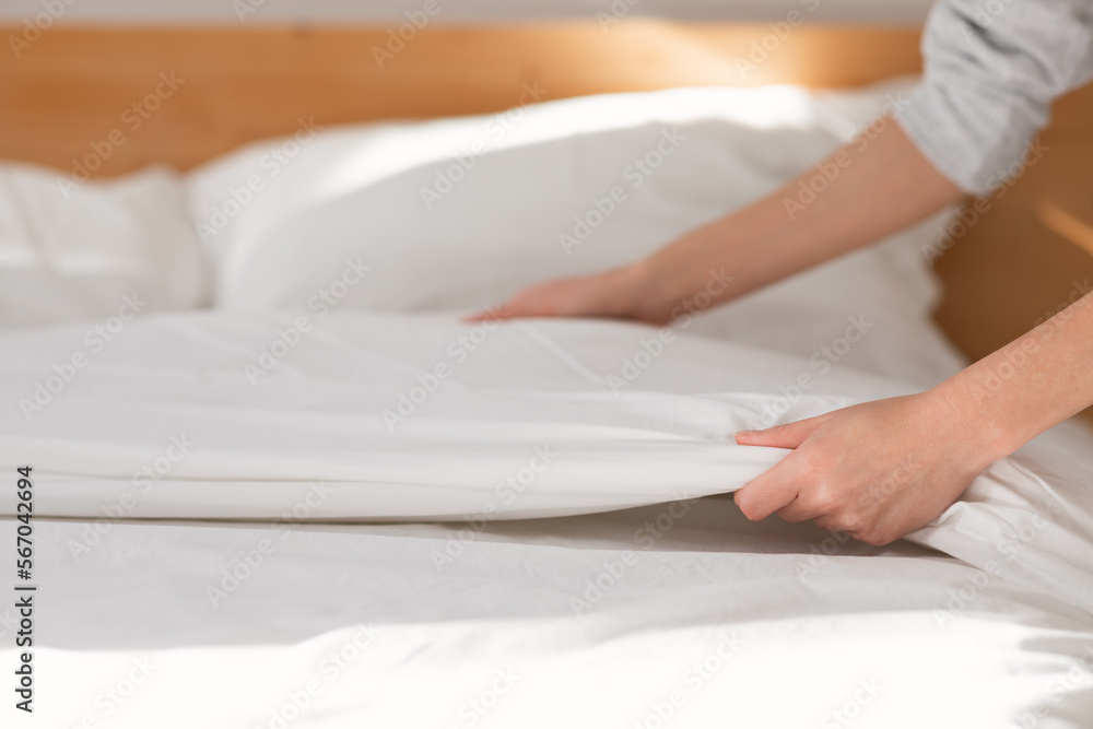 Hands of young european woman makes white bed with blanket in bedroom interior, close up Hands of young european woman makes white bed with blanket in bedroom interior, close up