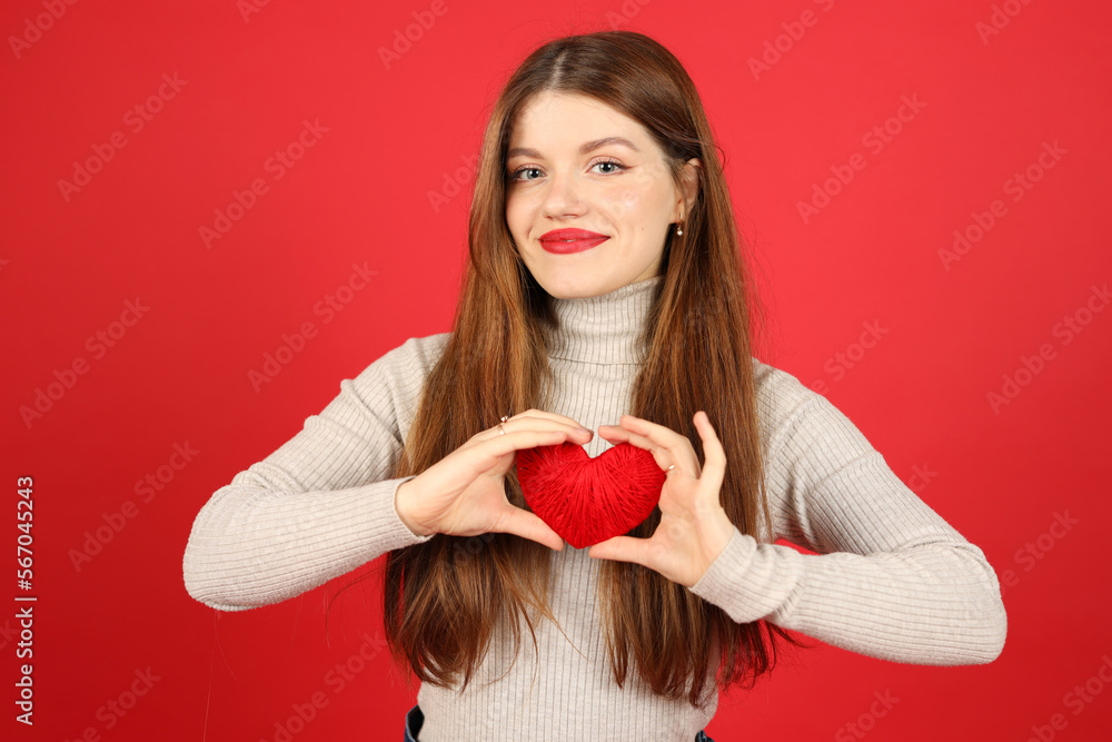 A young woman holds a heart in her hands on a red background, a blood donor. Valentine's Day. A young woman holds a heart in her hands on a red background, a blood donor. Valentine's Day.