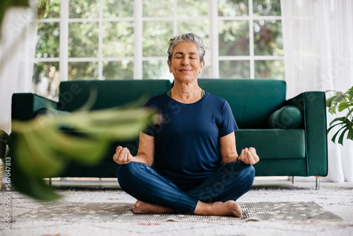 Relaxing the mind and finding inner peace with yoga: Senior woman meditating at home photo