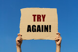 Try again message on box paper held by 2 hands with blue sky background. This note can be used for business concept about encouraging people to try again.