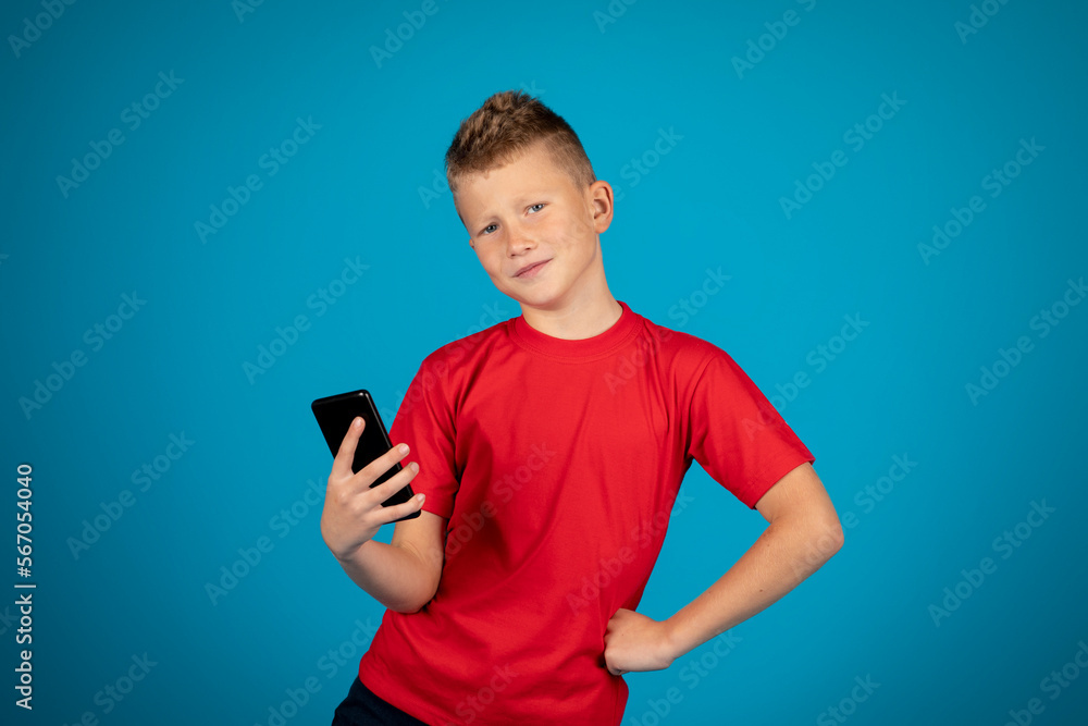 Smiling Preteen Boy With Smartphone In Hand Standing On Blue Studio Background Smiling Preteen Boy With Smartphone In Hand Standing On Blue Studio Background